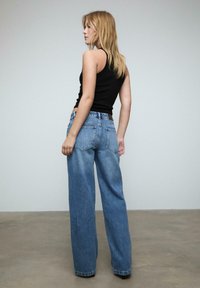 Breda ben blå denimjeans med en urtvättad finish och en svart linne. Har bakfickor och en klassisk fem-fickorsdesign.