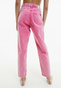 Jeans de mezclilla rosa con una cintura alta, corte recto y bolsillos traseros visibles. Cuenta con una etiqueta de marca en la cintura.