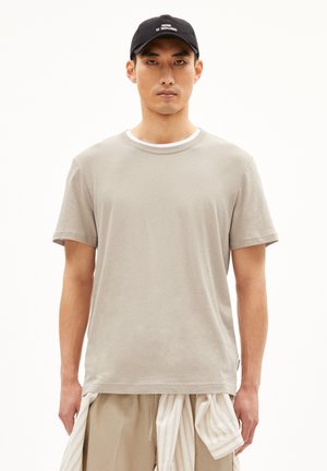Light gray short-sleeve t-shirt with a crew neck and white inner collar, made of soft fabric. Paired with beige pants and a black cap.