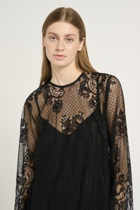 Svart spetsklänning med en genomskinlig, strukturerad design med blommönster och långa ärmar. Den lager-på-lager-stil inkluderar en solid underklänning.