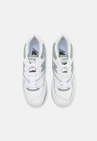 Vue de dessus de baskets New Balance 550 blanches et vert clair avec lacets attachés, placées côte à côte sur un fond uni.