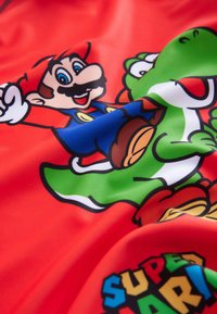 Red fabric featuring a vibrant print of a character with a blue outfit and a green dinosaur, surrounded by colorful text and accents.