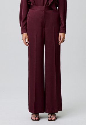 Pantaloni larghi bordeaux in tessuto liscio, a vita alta e con pieghe, abbinati a sandali neri con cinturini.