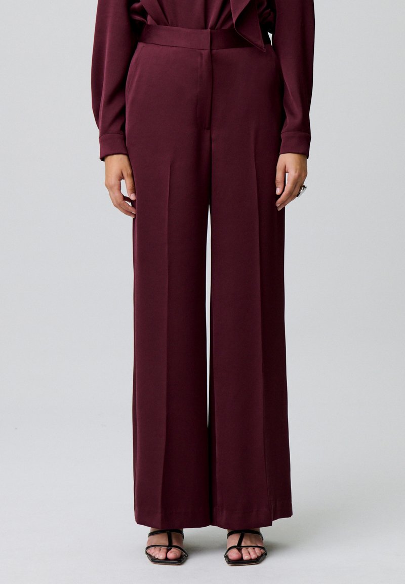 Pantaloni larghi bordeaux in tessuto liscio, a vita alta e con pieghe, abbinati a sandali neri con cinturini.