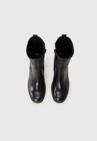 Bottes de cheville en cuir noir au design épuré, bout rond, talon bas et zips sur les côtés. Texture lisse avec de subtils détails de couture.