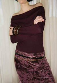 Haut bordeaux à épaules dénudées associé à une jupe violette texturée ornée d'un motif floral, rehaussé par une ceinture noire et dorée.