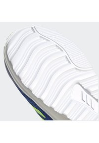 Suola di scarpa con una superficie in gomma bianca dotata di profonde scanalature e righe per una migliore aderenza, attaccata a una tomaia in tessuto blu con dettagli verdi.