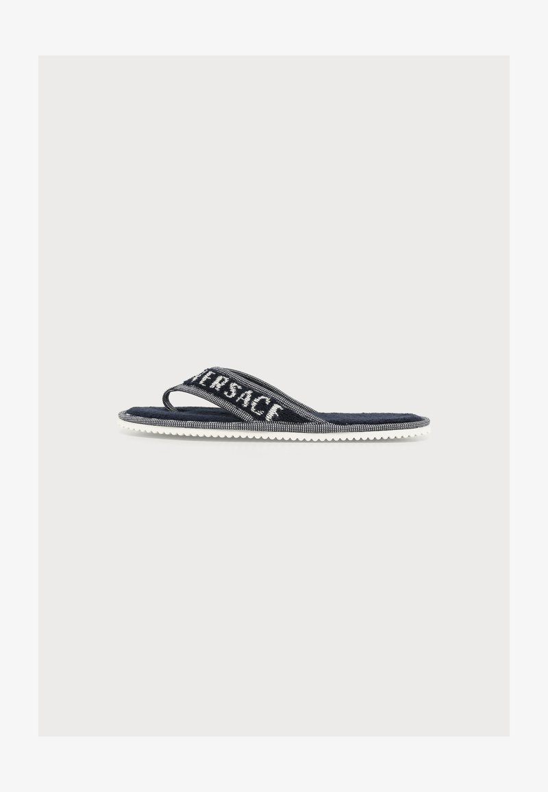 Sandale flip-flop noir et blanc avec une large bride en tissu affichant le nom de la marque "VERSACE" en lettres blanches.