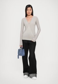 Light gray ribbed long-sleeve top with a V-neck, paired with black flared jeans and a small blue handbag with short handles and a tag.