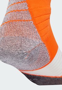 Oranžová športová ponožka s textúrovaným vzorom; má šedú pätu a biely pruh na špičke. Pletená tkanina navrhnutá na výkon.