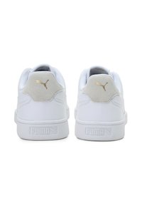 Ténis brancos com calcanhar em camurça cinza texturizado e detalhes dourados do logótipo da Puma. Parte superior em sintético suave e sola em borracha, projetados para conforto.