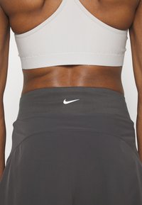 Pantalones cortos atléticos grises con una cinturilla ancha que presenta el logotipo de la marca Nike en blanco. El material parece suave y ajustado a la piel.