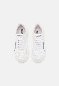Baskets blanches en cuir avec un bout perforé. Elles disposent de lacets plats, d'une forme arrondie et d'un accent noir sur le côté.