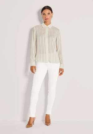 Doorschijnend, lichtbeige overhemd met verticale strepen, gecombineerd met nauwsluitende witte spijkerbroeken en nude hoge hakken.