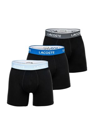Drei schwarze Lacoste Boxershorts mit elastischem Bund in Grau, Blau und Hellblau, jeweils mit dem Lacoste-Logo.