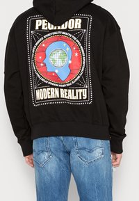 Schwarzer Kapuzenpullover mit einem farbenfrohen Grafikdruck auf der Rückseite, der Designelemente wie eine Weltkugel, Sterne und Text enthält.