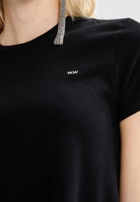 Černé bavlněné tričko s kulatým výstřihem, krátkými rukávy a malým bílým logem "W.W." na hrudi. Hladká textura, přiléhavý střih.