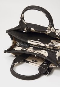 Borsa in cotone con un motivo di teschi nero e crema, dotata di due manici corti, una tasca con zip e una chiusura a scatto in metallo.