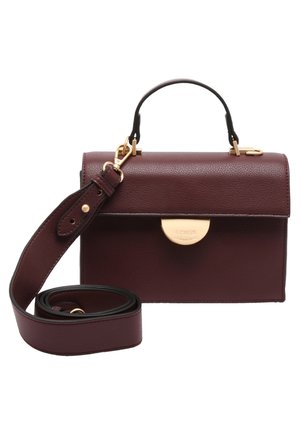 Sac à main en cuir marron foncé avec fermoir doré, poignée courte, et bandoulière longue ajustable détachable enroulée à côté du sac.