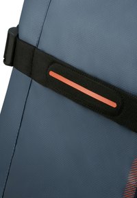 Närbild av ett svart justerbart band med en orange reflexrand på en texturerad blå stolrygg.