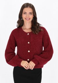 Röd stickad cardigan med rund hals, oversized ärmar och knappar som liknar pärlor. Mjuk textur och fyllig design.
