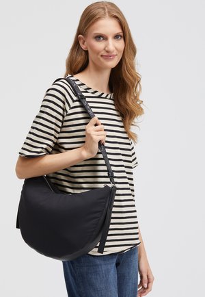 Schwarze Nylon-Hobo-Tasche mit glatter Textur, geschwungener Form und schmalem Tragegurt. Über die Schulter getragen, kombiniert mit einem gestreiften Hemd.