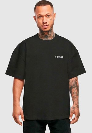 Black oversized t-shirt made of cotton, featuring a small white logo on the left chest and short sleeves, designed with a relaxed fit.