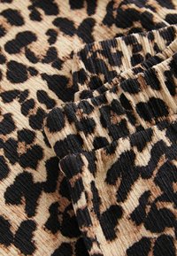 Tissu imprimé léopard présentant une texture côtelée dans des nuances de beige, noir et marron, avec des taches irrégulières distinctes et une finition douce.