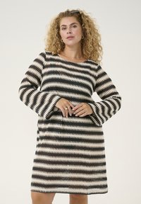 Abito lavorato a maglia con motivo a zigzag nei colori nero, crema e ruggine. Il design ha una vestibilità rilassata con maniche lunghe a campana svasate.