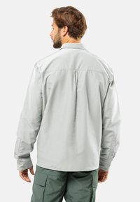 Camicia a maniche lunghe grigia chiaro con vestibilità rilassata, polsini con bottone e dettaglio sullo yoke posteriore, abbinata a pantaloni cargo verdi.