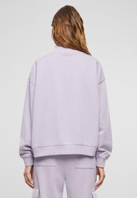 Lilafarbener Pullover mit hohem Kragen, überschnittenen Schultern und gerippten Bündchen. Das Material wirkt weich und bietet eine gemütliche, lockere Passform.