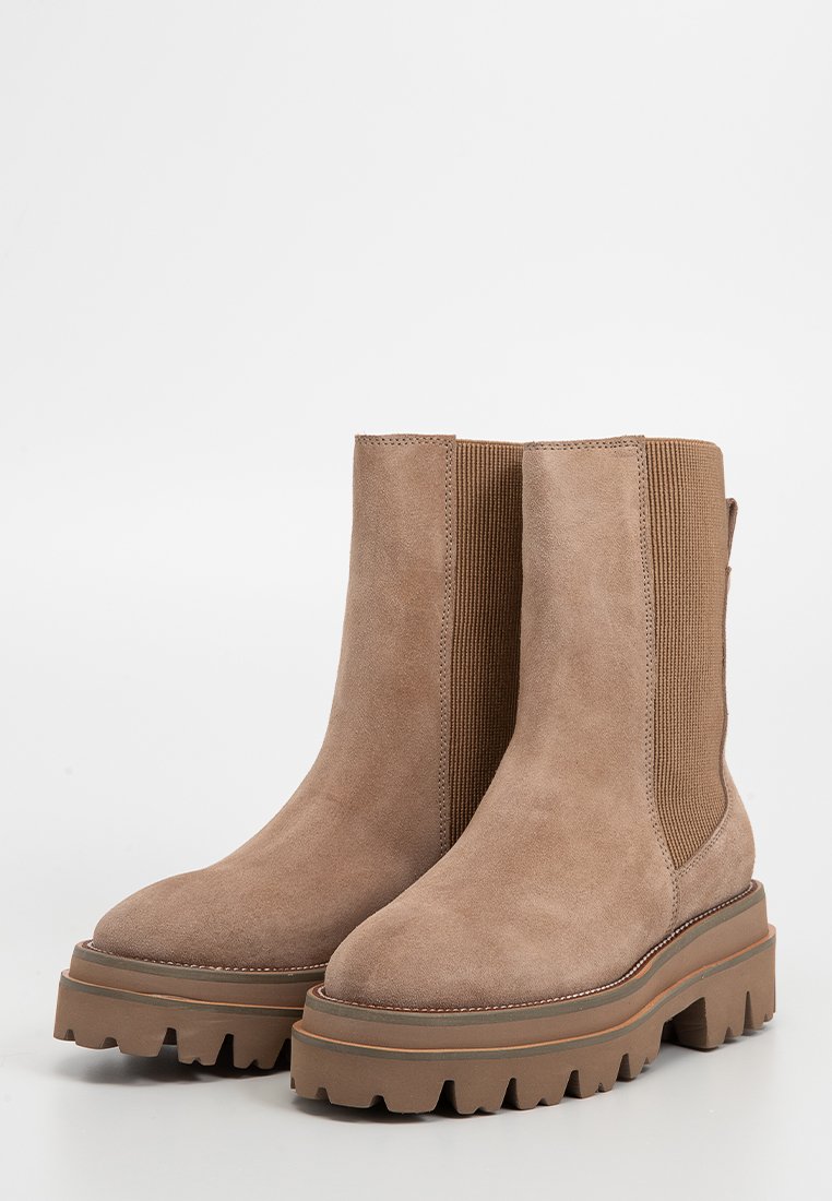 Braune Wildleder-Stiefeletten mit elastischen Seitenpartien, dickem Plateau und griffiger Sohle. Glatte Textur und abgerundete Zehenpartie.