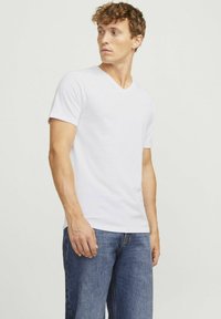 Weißes V-Ausschnitt-T-Shirt aus weichem Baumwollmaterial, mit kurzen Ärmeln und entspannter Passform, kombiniert mit blauen Jeans.