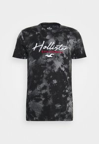 Svart tie-dye bomull t-shirt med rund halsringning. Har "Hollister CALIFORNIA" i vit och röd text över framsidan. Kortärmad.
