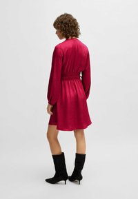 Red satin dress with long sleeves, gathered waist, and flared hem. Paired with black suede knee-high boots.