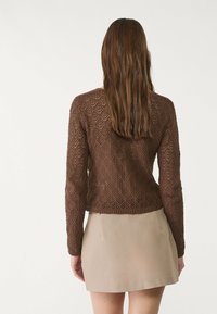 Maglione marrone lavorato a maglia con maniche lunghe, caratterizzato da un motivo a rombi aperto, abbinato a una gonna beige chiaro sopra il ginocchio.