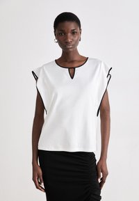 Hvit kortermet topp med svarte detaljer, med en nøkkelhull-neckline og en avslappet passform, parret med et svart rynket skjørt.