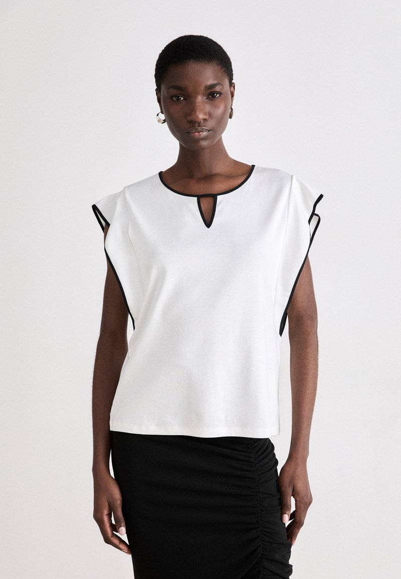 Hvit kortermet topp med svarte detaljer, med en nøkkelhull-neckline og en avslappet passform, parret med et svart rynket skjørt.