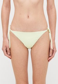 Lichtgroene bikini onderkant met strikaccenten aan de zijkanten, met een gladde textuur en een ontwerp met minimale bedekking.