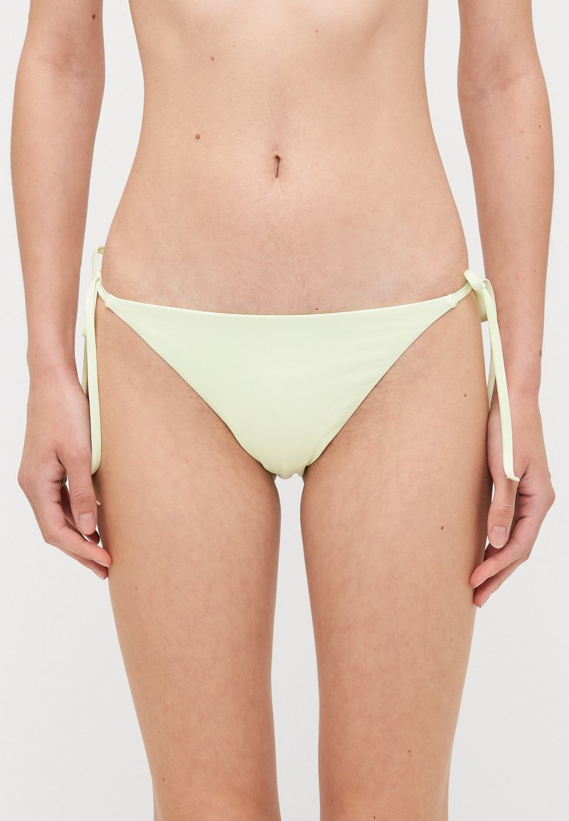 Lichtgroene bikini onderkant met strikaccenten aan de zijkanten, met een gladde textuur en een ontwerp met minimale bedekking.