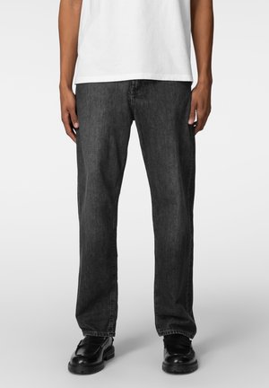 Mørkegrå denimjeans med løs passform, rette ben og synlige sømmer. Brukt med svarte sko og sammen med en hvit t-skjorte.