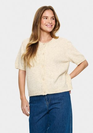 Cardigan beige à manches courtes, en tissu tricoté texturé, col rond, fermeture à boutons, coupe décontractée, associé à un jean large bleu.