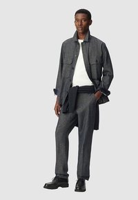 Ciemnoszara, teksturowana wełniana kurtka z dwoma przednimi kieszeniami, noszona na białej bluzce, w zestawie z pasującymi spodniami i czarnymi butami.