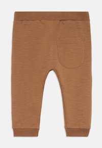 Brune bukser laget av myk stoff, med en ribbestrikket midje, avsmalnende ben og en enkel baklomme med hemede mansjetter.