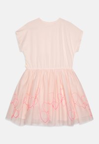Robe rose avec un haut en coton doux et une jupe en tulle transparente. La jupe présente des contours de cœurs roses en détail décoratif. Manches courtes, décolleté rond.