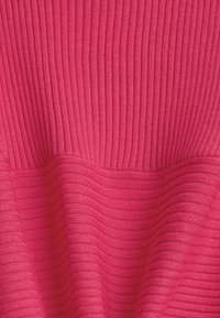 Gros plan sur un tissu en tricot côtelé rose vif montrant des motifs texturés verticaux et horizontaux.
