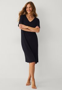 Czarna sukienka z krótkim rękawem i dekoltem w kształcie litery V, z koronkowym wykończeniem na rękawach, wykonaną z miękkiego materiału i luźnym krojem, który sięga do połowy łydki.