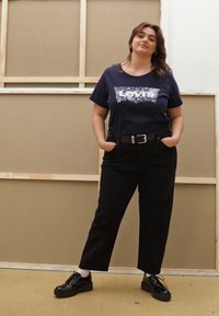 T-shirt marine avec un logo "Levi's" en fleurs blanches, associé à un pantalon noir taille haute et des chaussures à lacets noires à finition brillante.