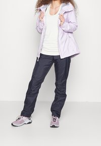 Světle fialová voděodolná bunda s kapucí, v kombinaci s námořnickými voděodolnými kalhotami a světle růžovými sportovními botami s výkonným designem.