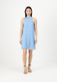 Light blue halter dress with a textured pattern of small dots, flowing fabric, and a mid-thigh length, paired with brown strappy sandals.